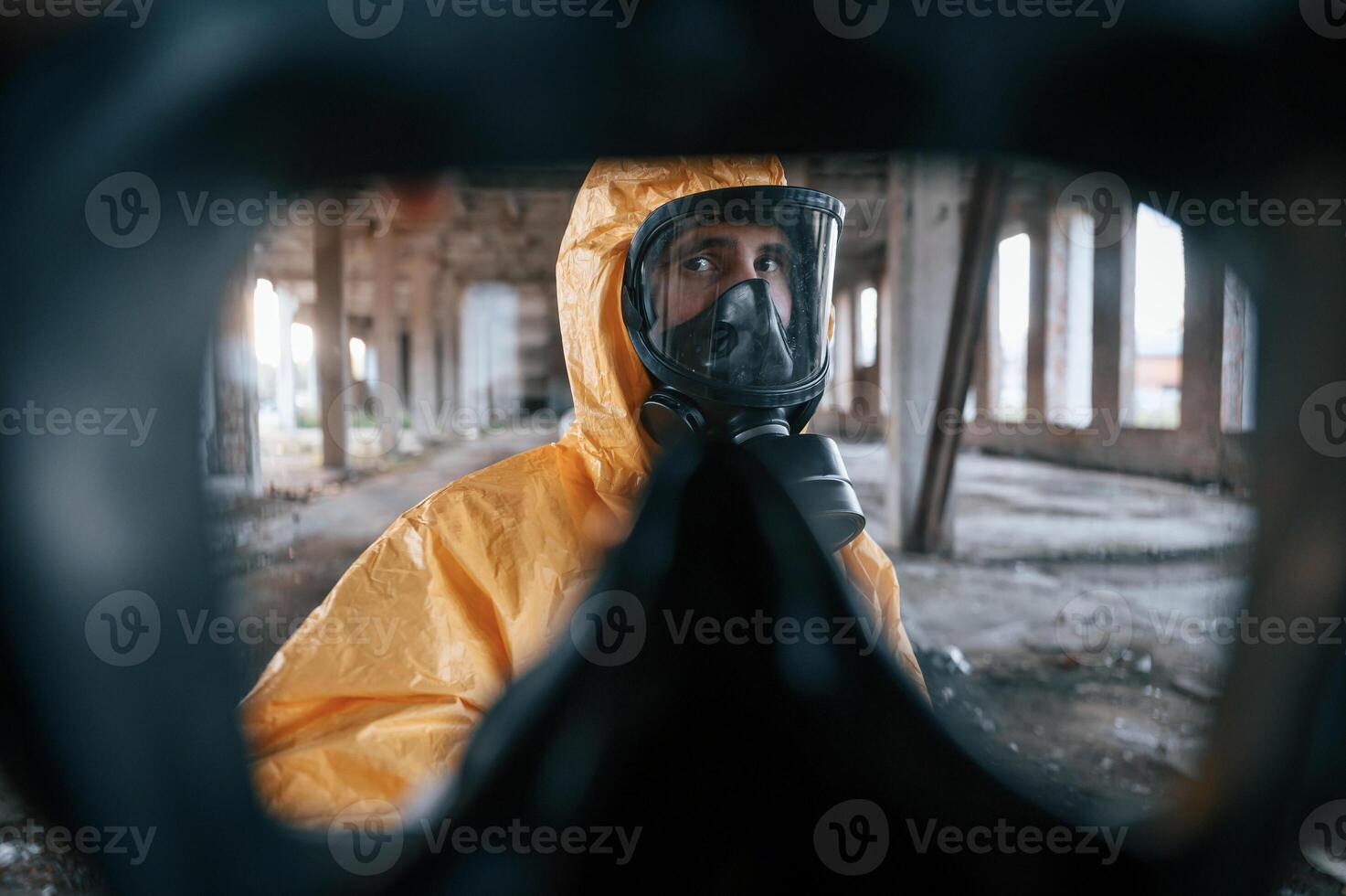 First, person view through respirator. Man dressed in chemical protection suit in the ruins of the post apocalyptic building photo