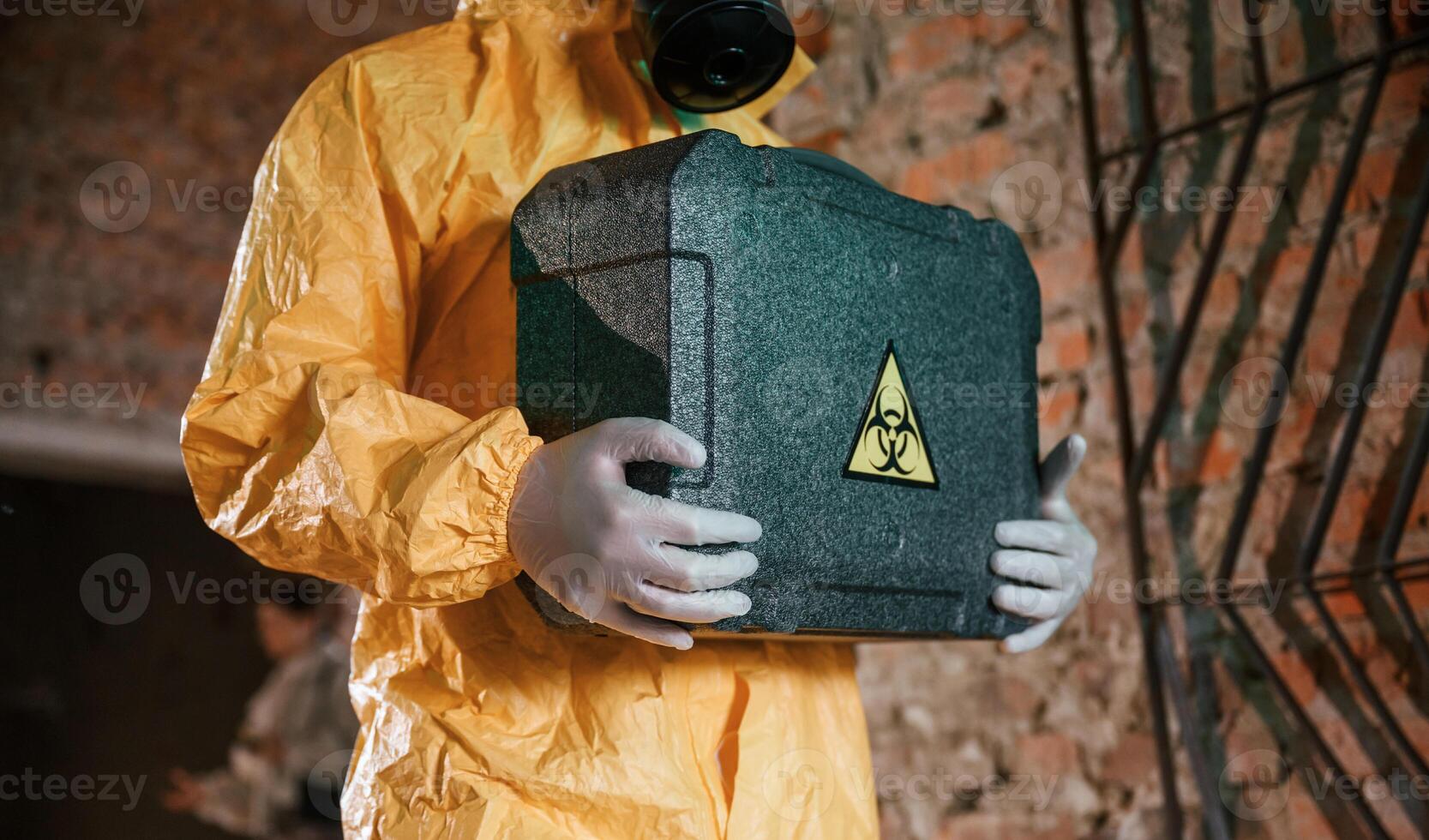 Case with ,biohazard sign in hands. Man dressed in chemical protection suit in the ruins of the post apocalyptic building photo
