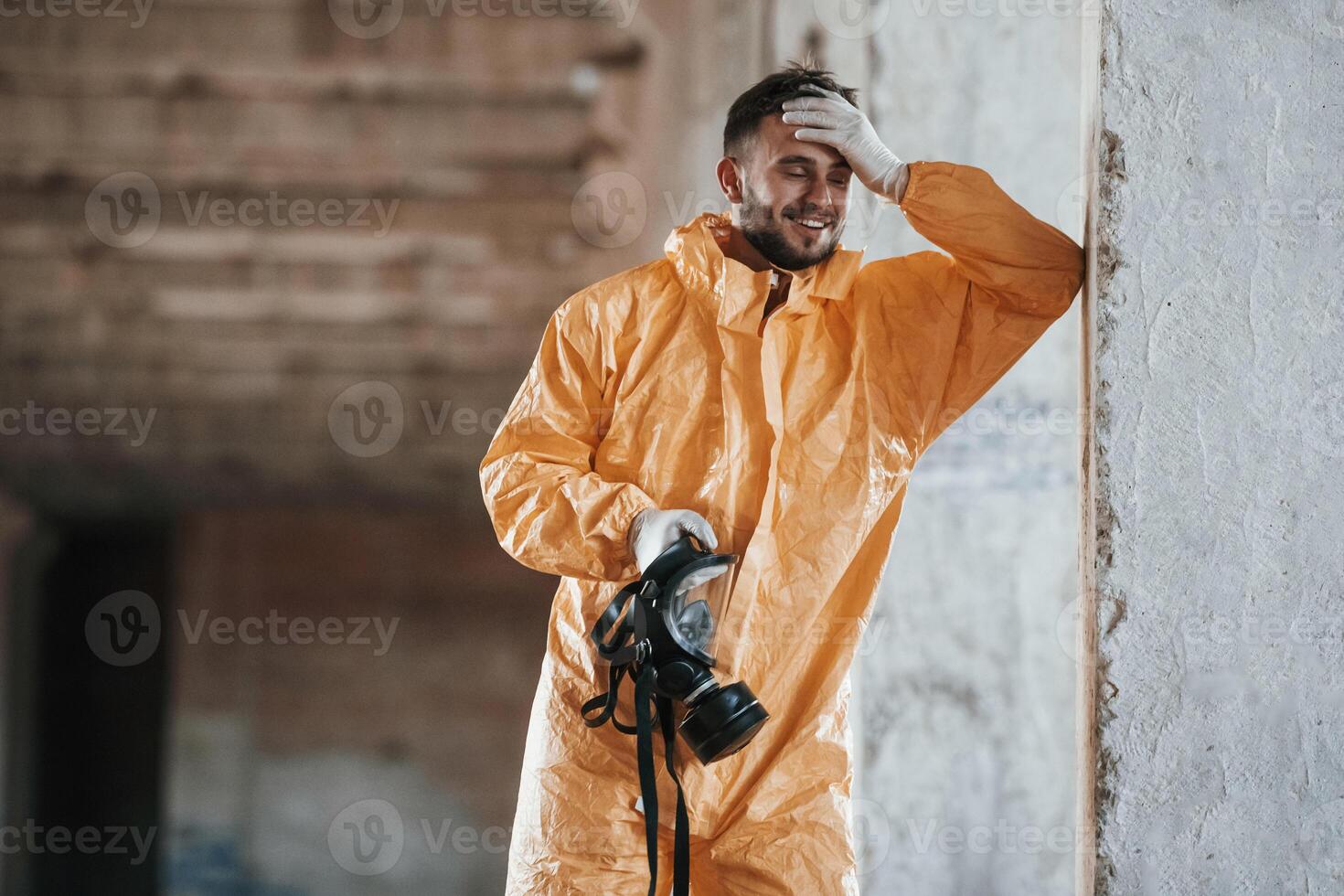 Holding, a respirator. Man dressed in chemical protection suit in the ruins of the post apocalyptic building photo