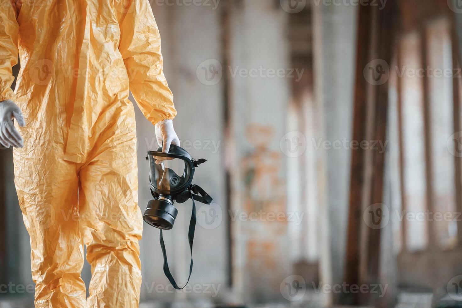 Respirator ,in hand.. Man dressed in chemical protection suit in the ruins of the post apocalyptic building photo
