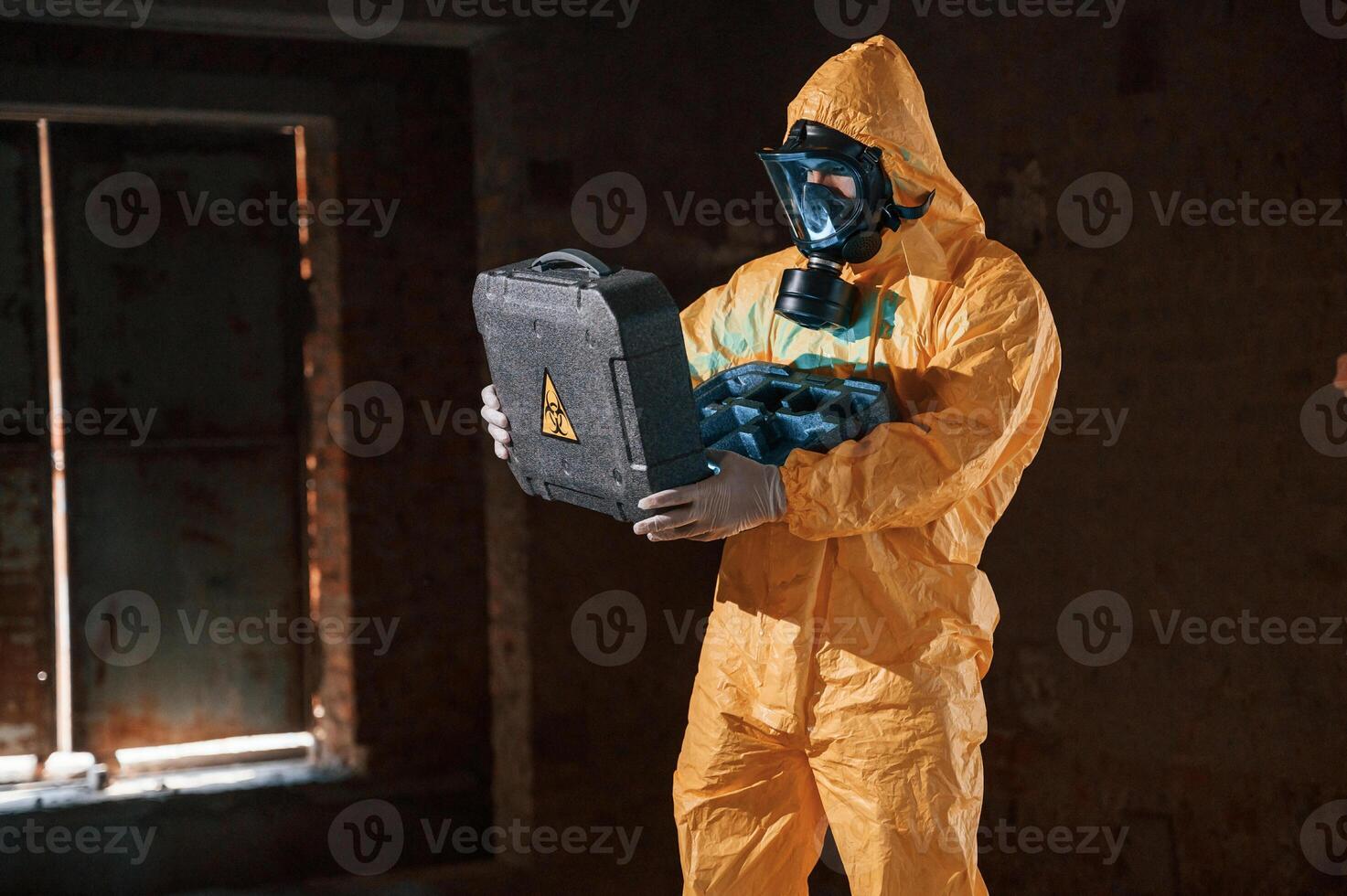 Blue light is, going from hard case that is with hazard sign. Man dressed in chemical protection suit in the ruins of the post apocalyptic building photo