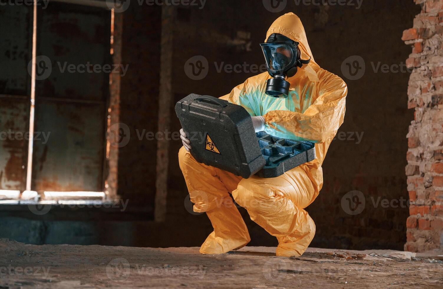 Case with blue ,glowing light. Hazard materials. Man dressed in chemical protection suit in the ruins of the post apocalyptic building photo