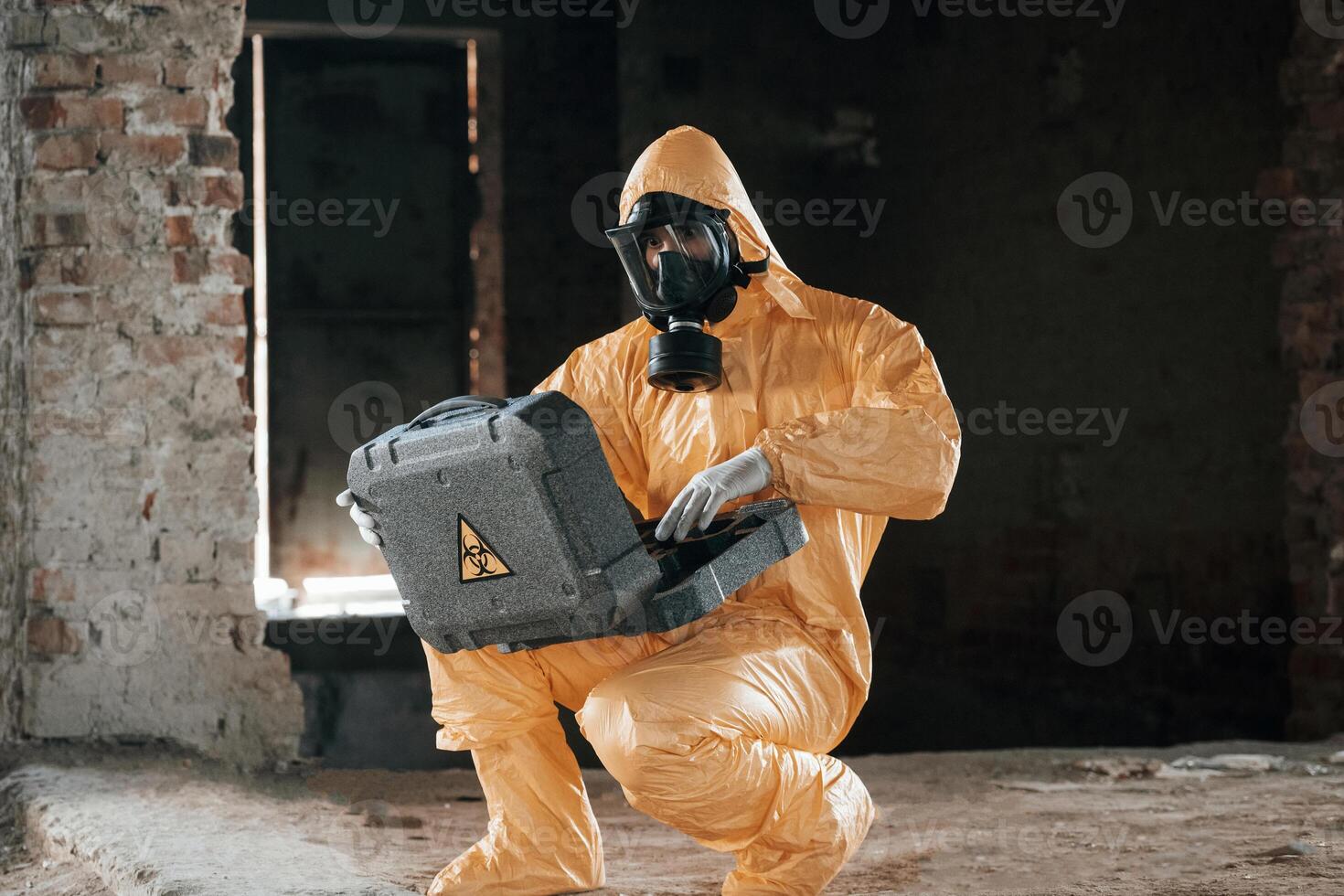 Sitting with radioactive, case. Man dressed in chemical protection suit in the ruins of the post apocalyptic building photo