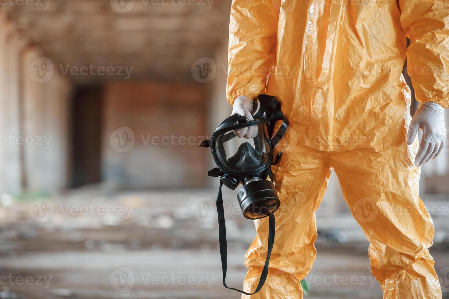 Holding gas mask. Man, dressed in chemical protection suit in the ruins of the post apocalyptic building photo