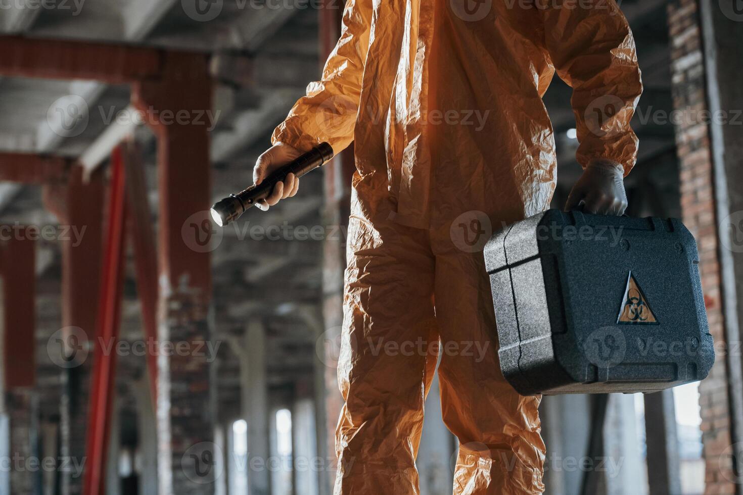 Holding case and flashlight.. Man dressed in chemical protection suit in the ruins of the post apocalyptic building photo