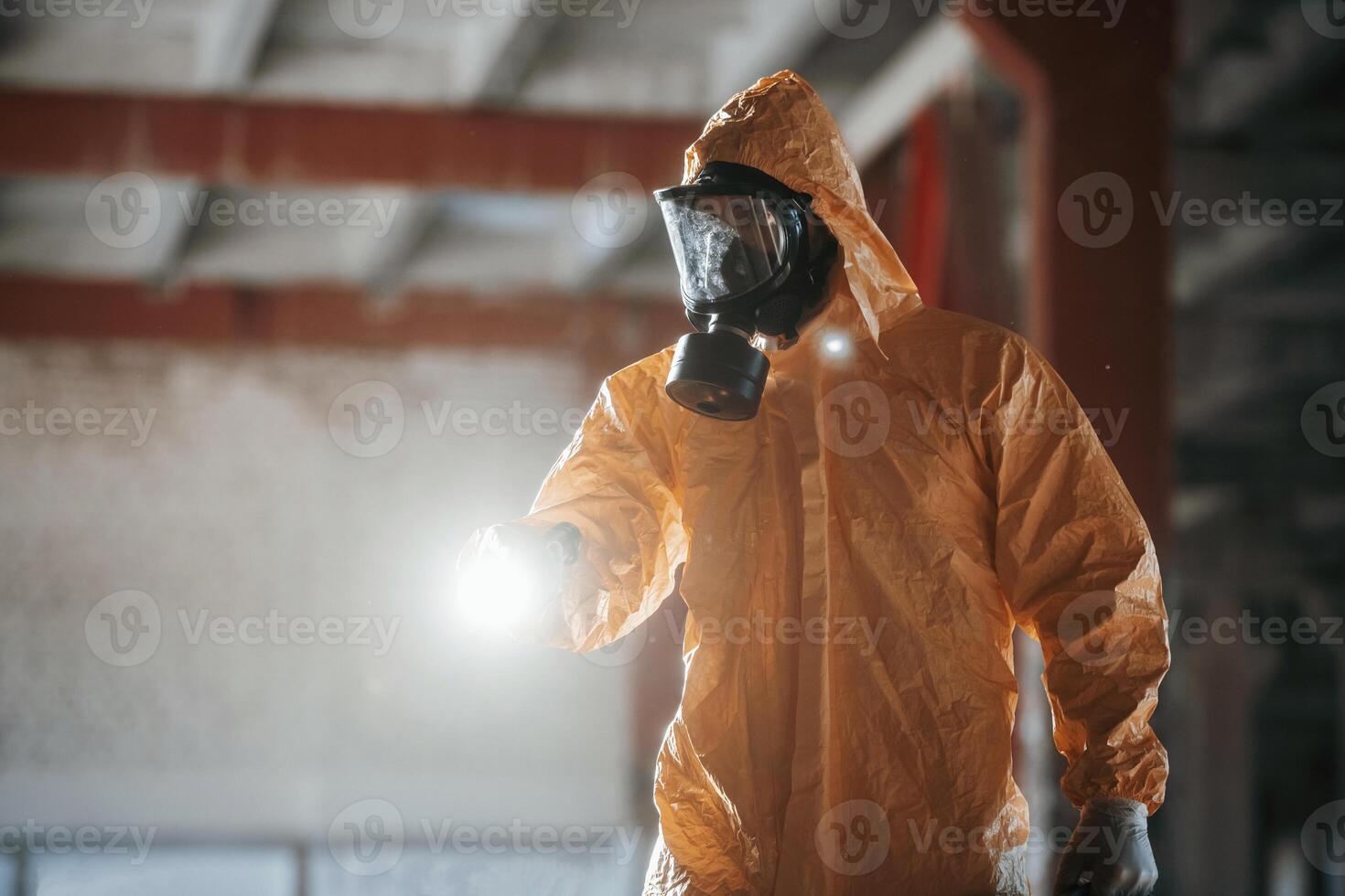 With flashlight. .Man dressed in chemical protection suit in the ruins of the post apocalyptic building photo