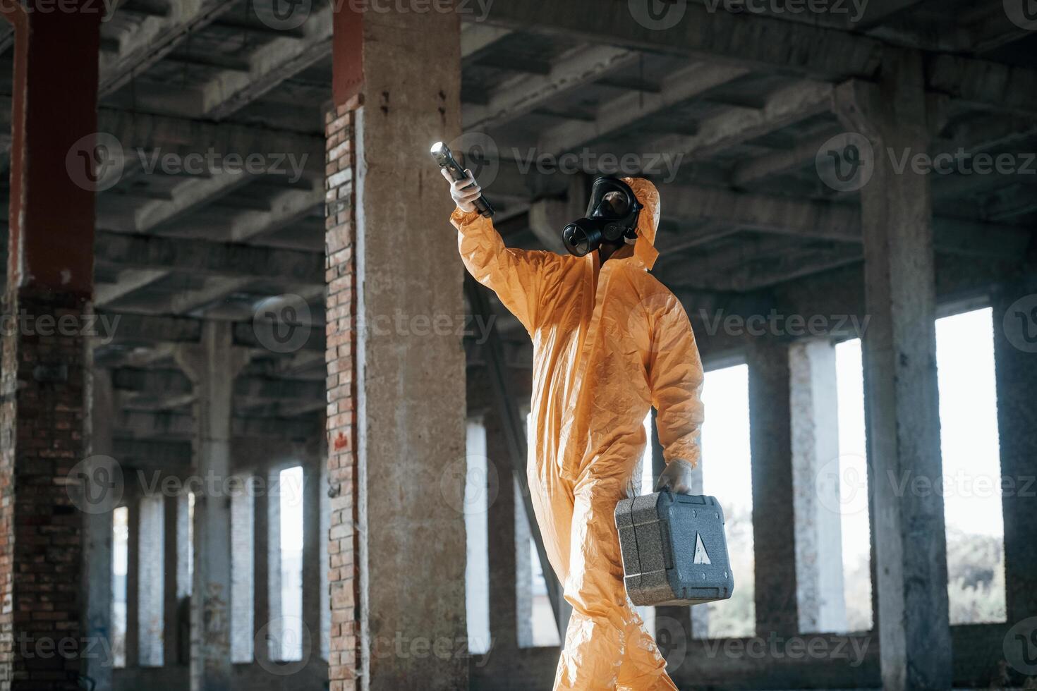 With flashlight.. Man dressed in chemical protection suit in the ruins of the post apocalyptic building photo