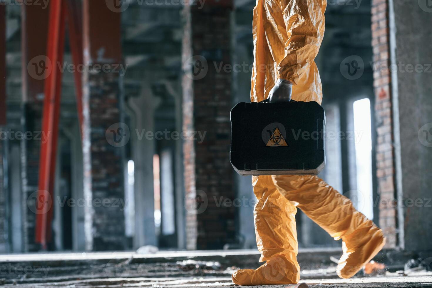 The case ,with, biohazard sign on it. Man ,dressed in chemical protection suit in the ruins of the post apocalyptic building photo