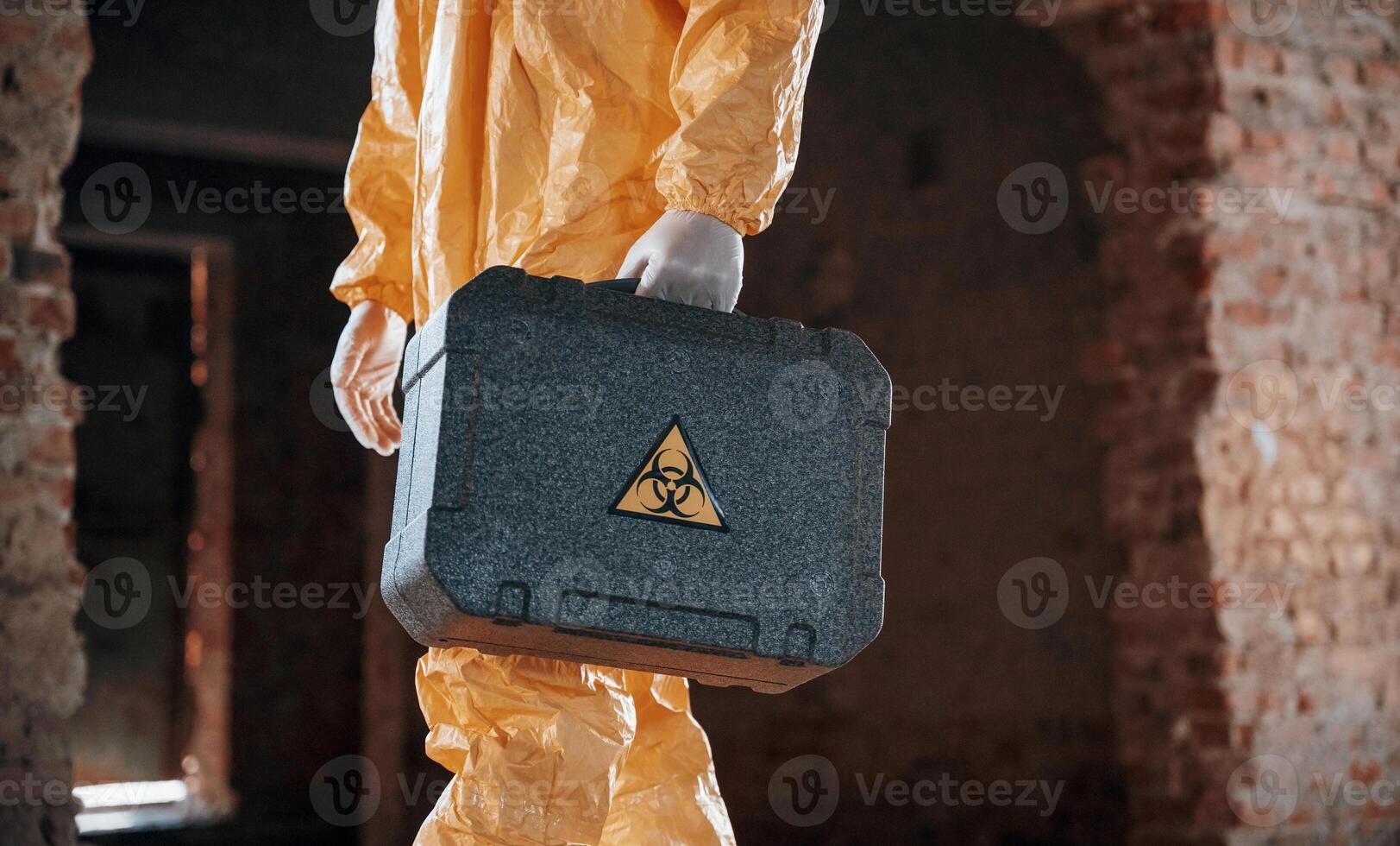 Case with, biohazard sign in hands. Man dressed in chemical protection suit in the ruins of the post apocalyptic building photo