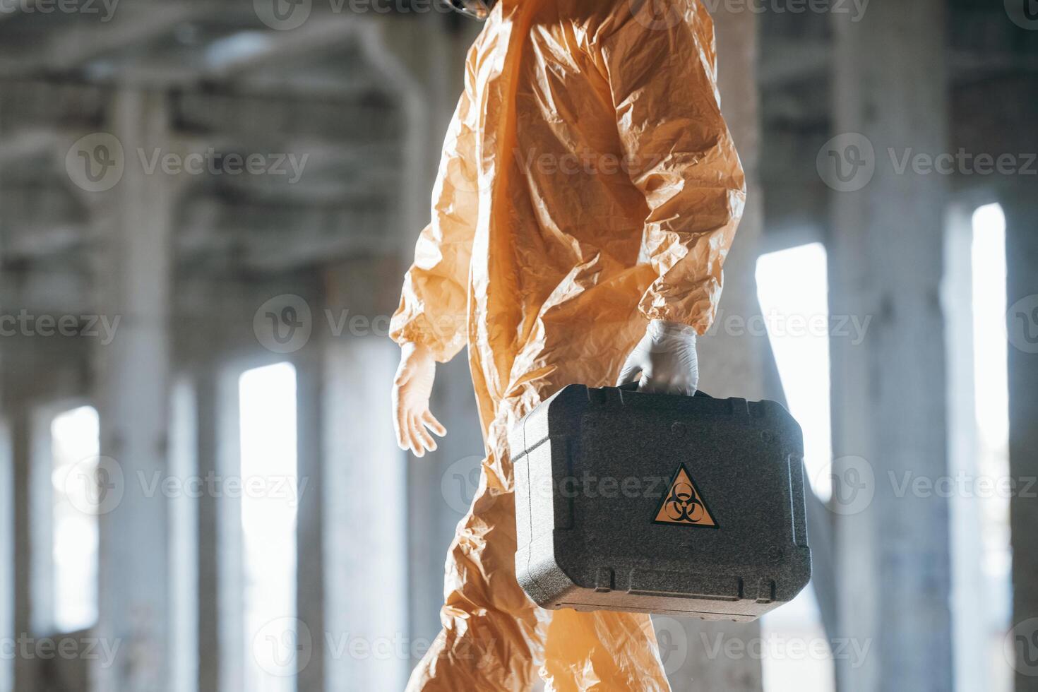 The case with ,biohazard sign on it. Man dressed in ,chemical protection suit in the ruins of the post apocalyptic building photo