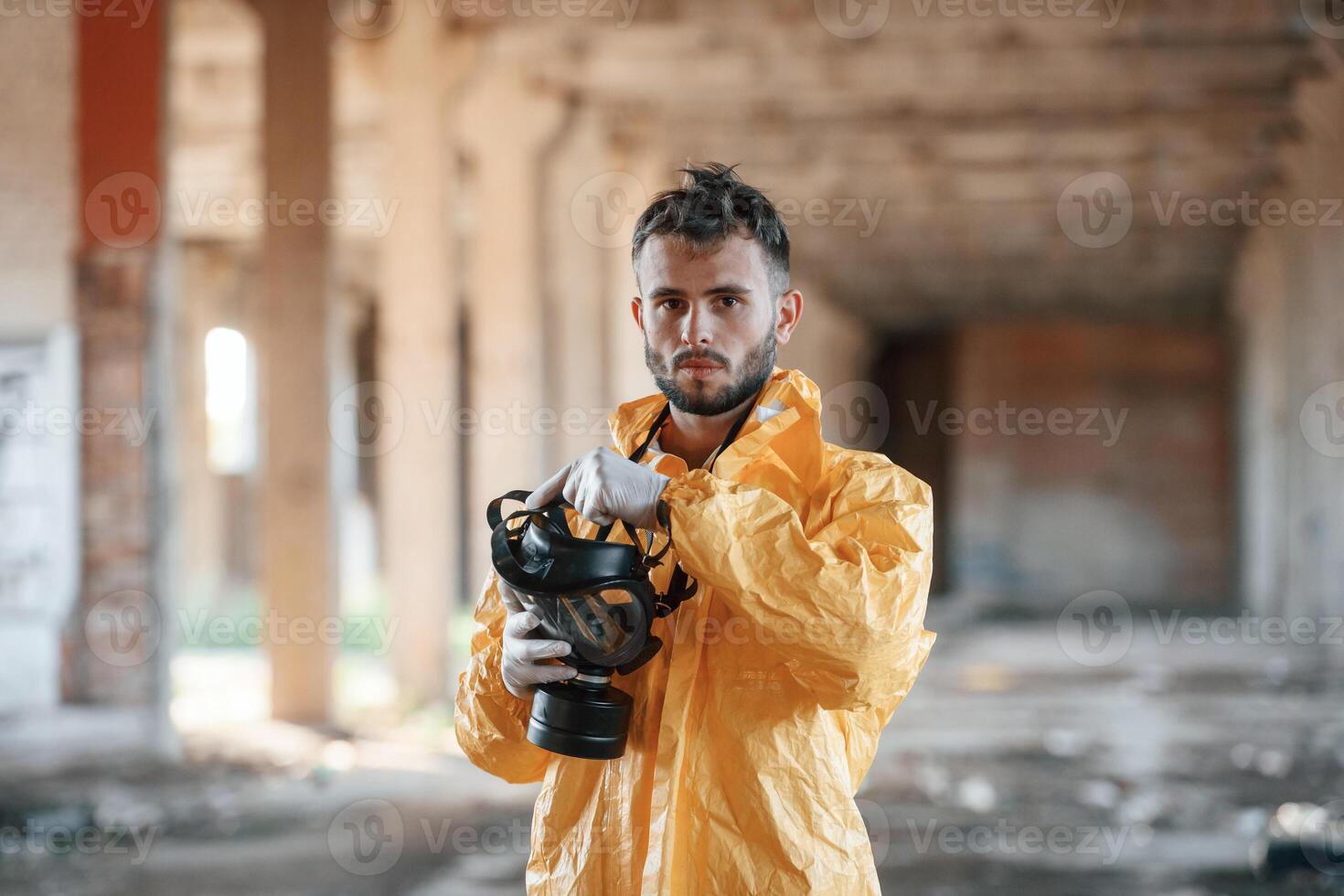Holding, gas mask. Man dressed in chemical protection suit in the ruins of the post apocalyptic building photo