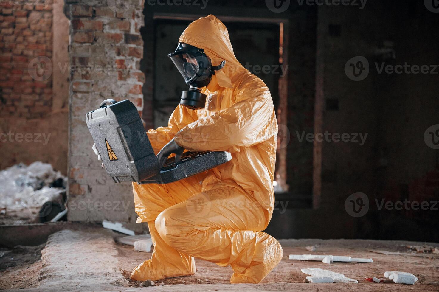 Sitting with, radioactive case. Man dressed in chemical protection suit in the ruins of the post apocalyptic building photo