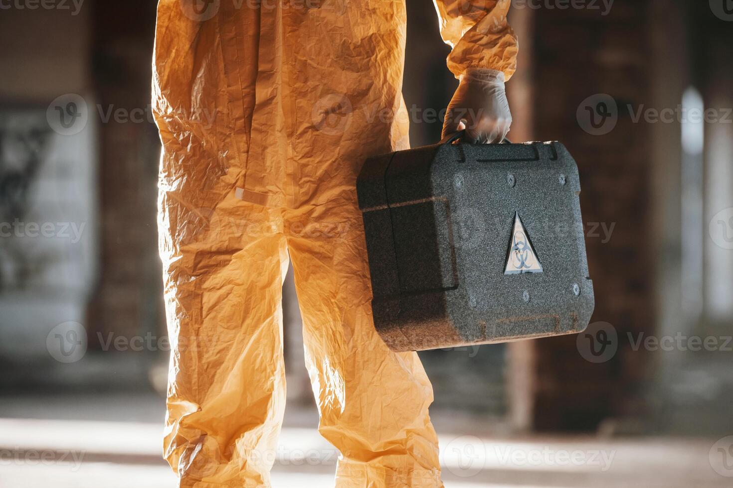 Holding ,case and flashlight. Man dressed in chemical protection suit in the ruins of the post apocalyptic building photo
