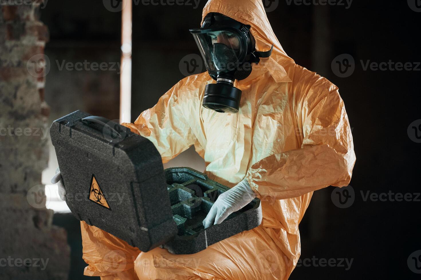 Case with blue glowing light. Hazard, materials. Man dressed in chemical protection suit in the ruins of the post apocalyptic building photo