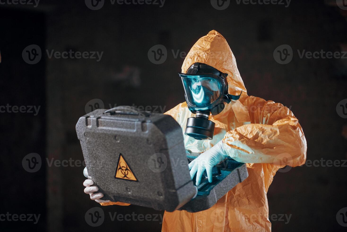 Case with, blue glowing light. Hazard materials. Man dressed in chemical protection suit in the ruins of the post apocalyptic building photo