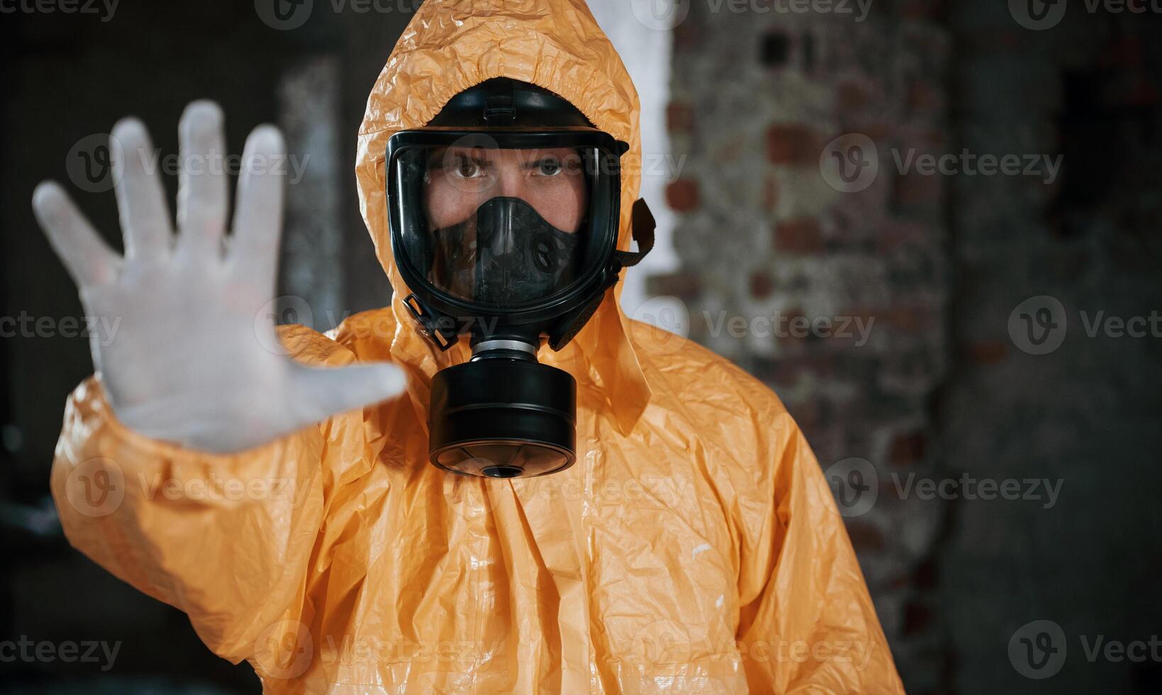 Stop sign, by hand. Man ,dressed in chemical protection suit in the ruins of the post apocalyptic building photo
