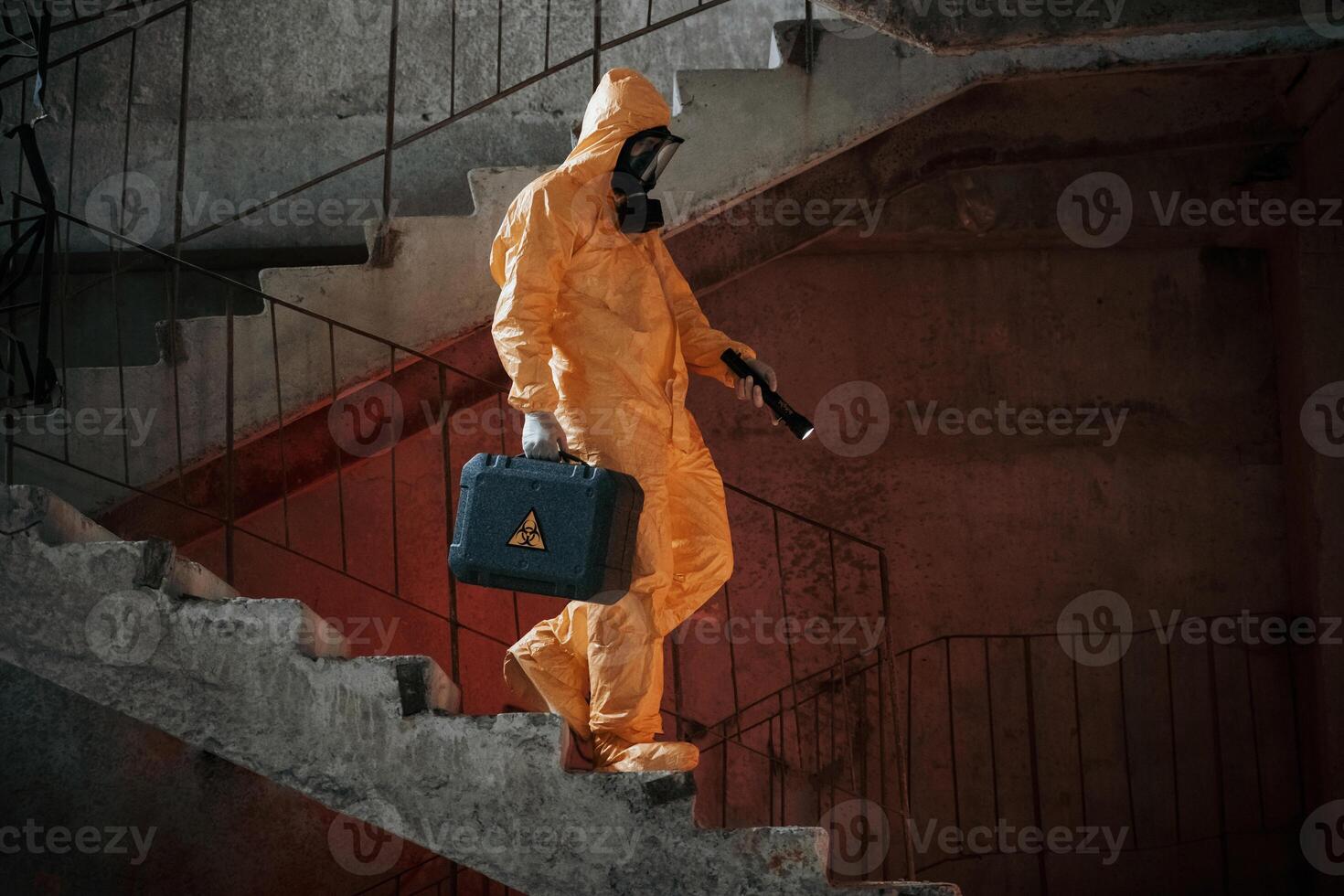 On ,stairs with flashlight and case. Man dressed in chemical protection suit in the ruins of the post apocalyptic building photo