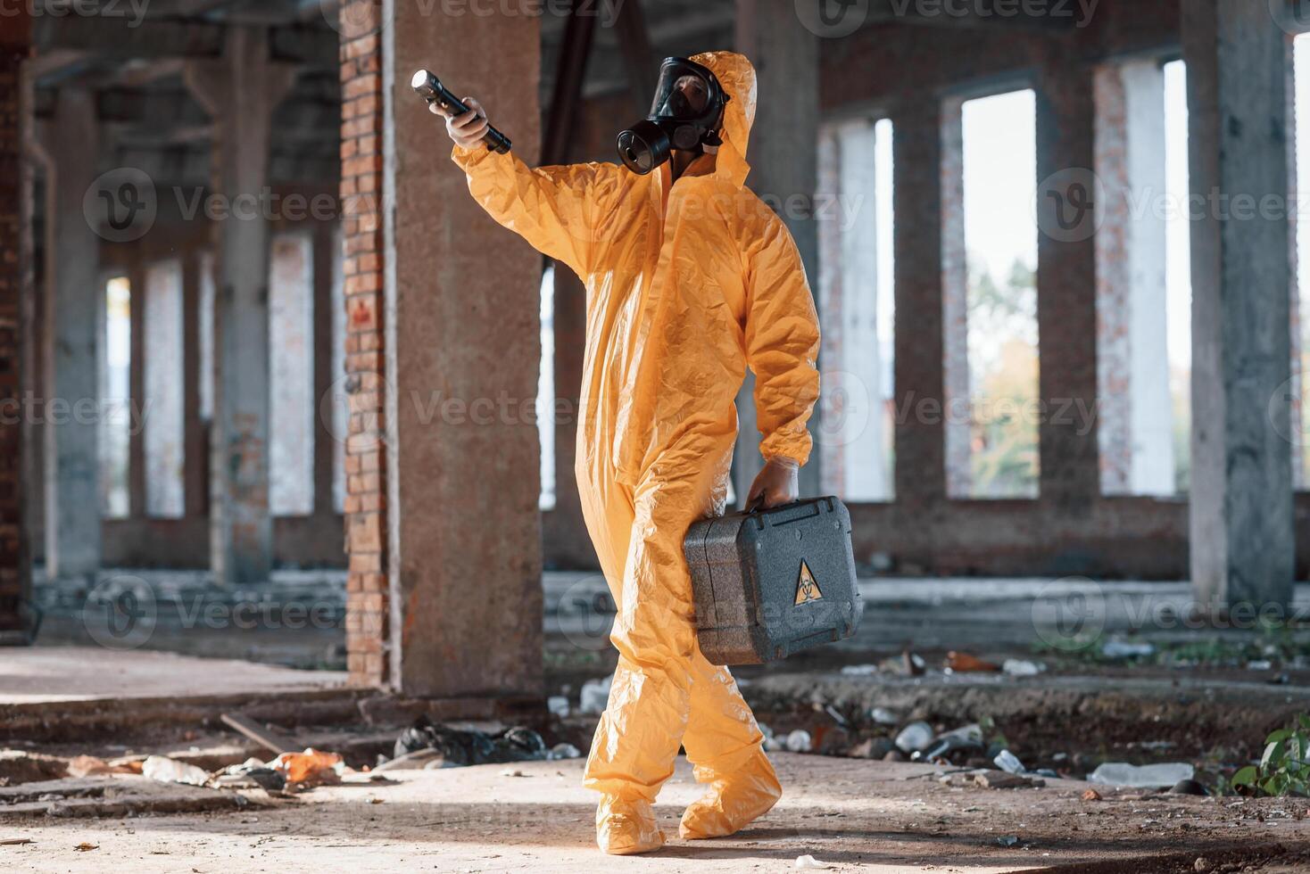 View from the side.. Man dressed in chemical protection suit in the ruins of the post apocalyptic building photo