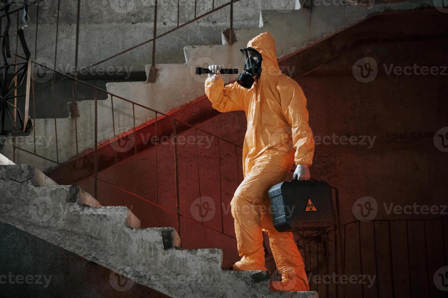 On stairs with flashlight and case. Man dressed in chemical protection suit in the ruins of the post apocalyptic building photo