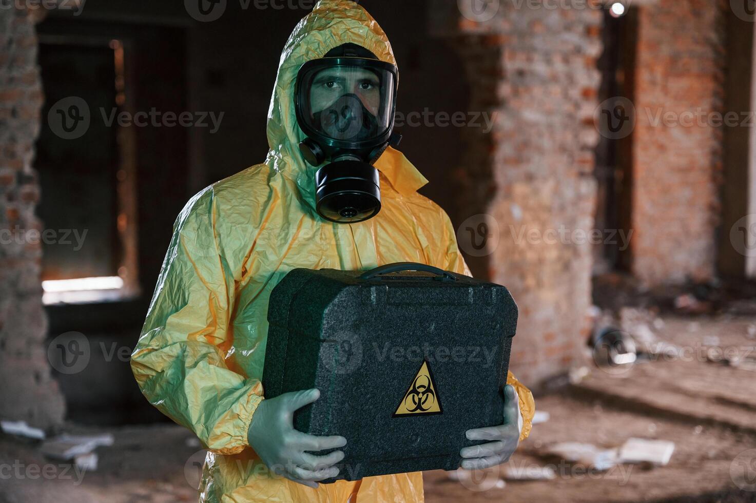 Case ,with biohazard sign in hands. Man dressed in chemical protection suit in the ruins of the post apocalyptic building photo