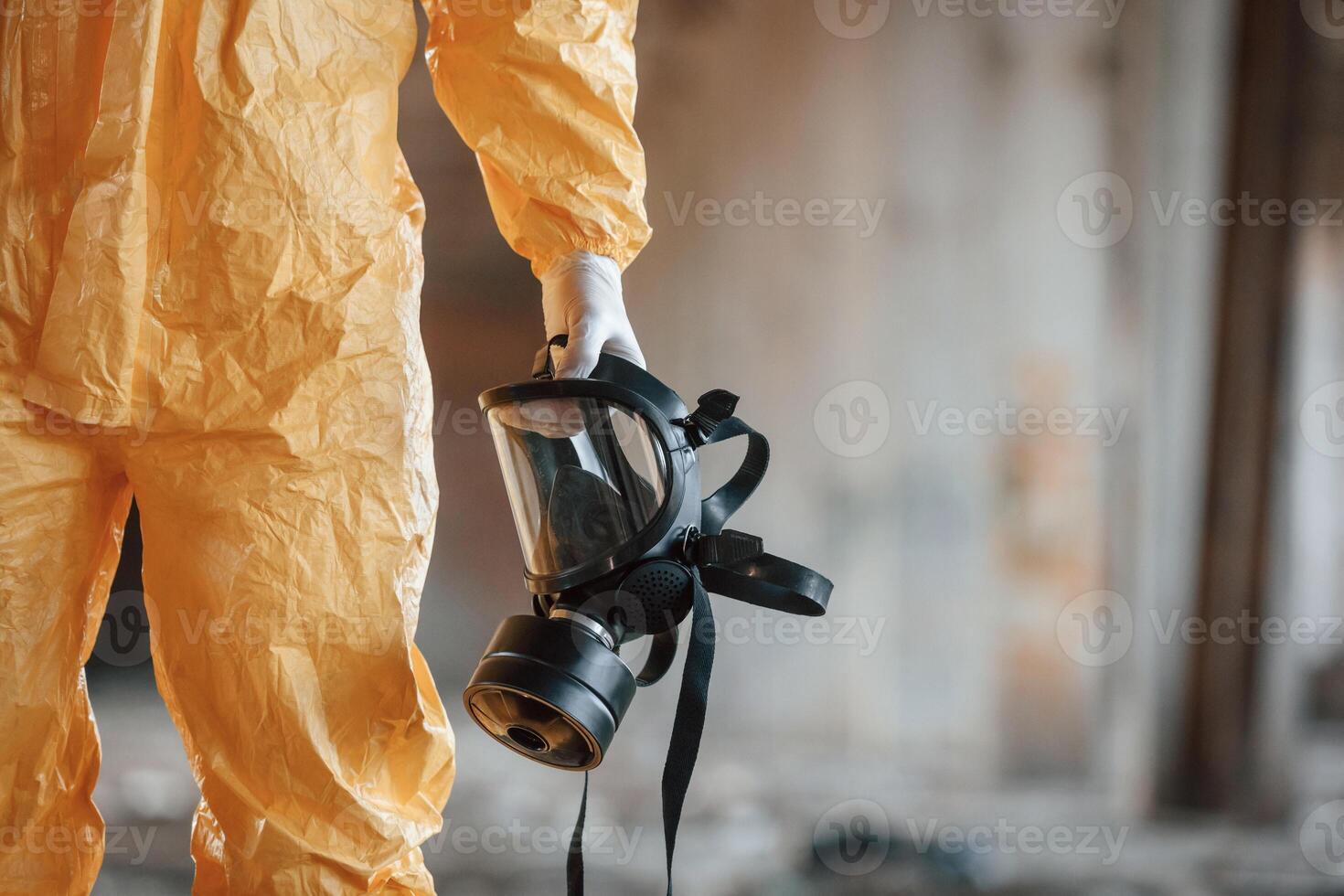 Holding gas mask. Man dressed in chemical protection suit in the ruins of the post apocalyptic building photo