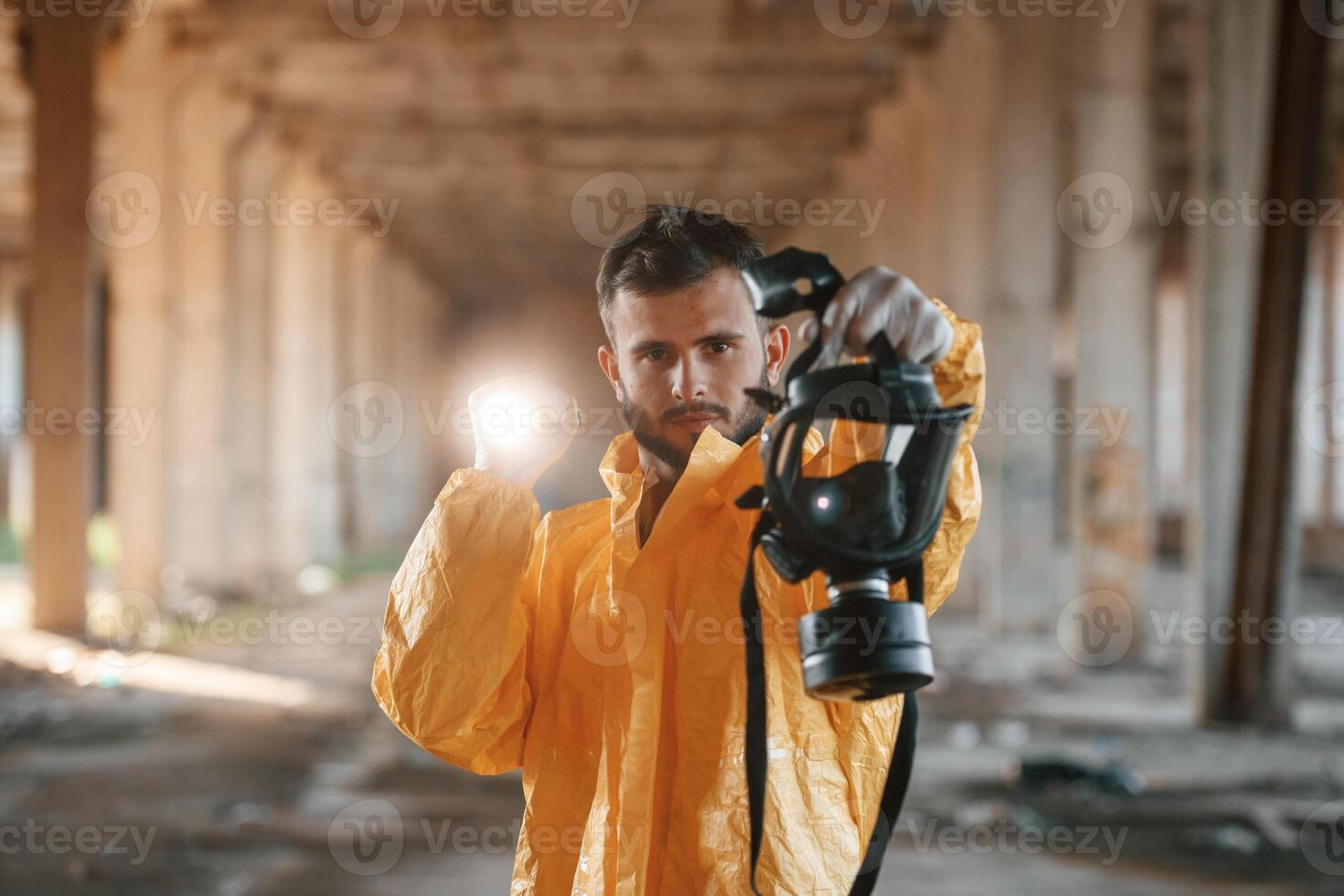 Holding a respirator. Man dressed in chemical protection suit in the ruins of the post apocalyptic building photo