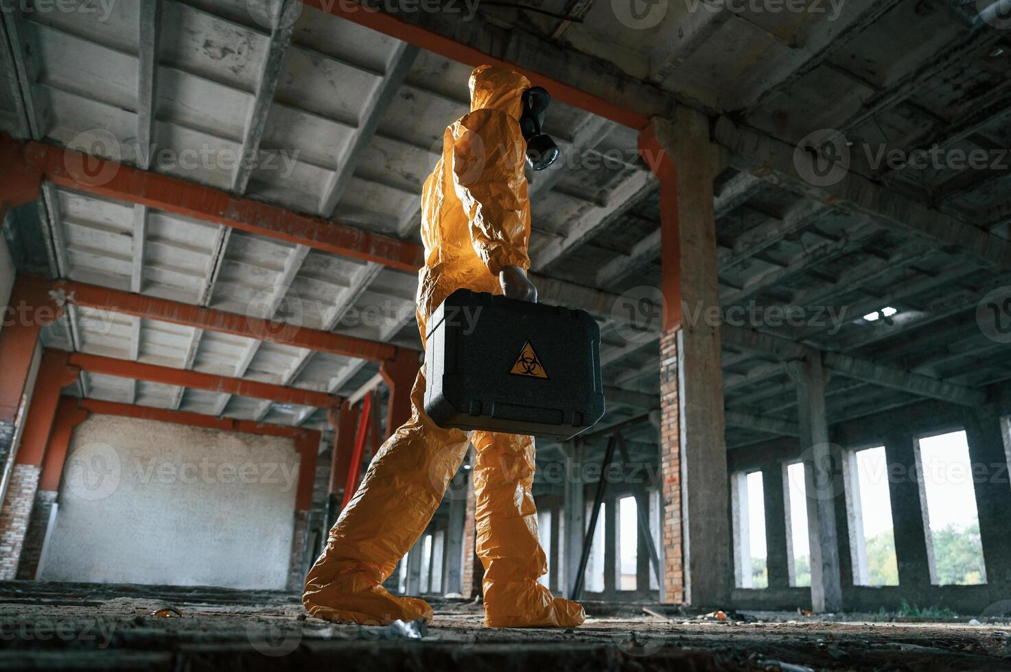 Walking with hard, case. Man dressed in chemical protection suit in the ruins of the post apocalyptic building photo