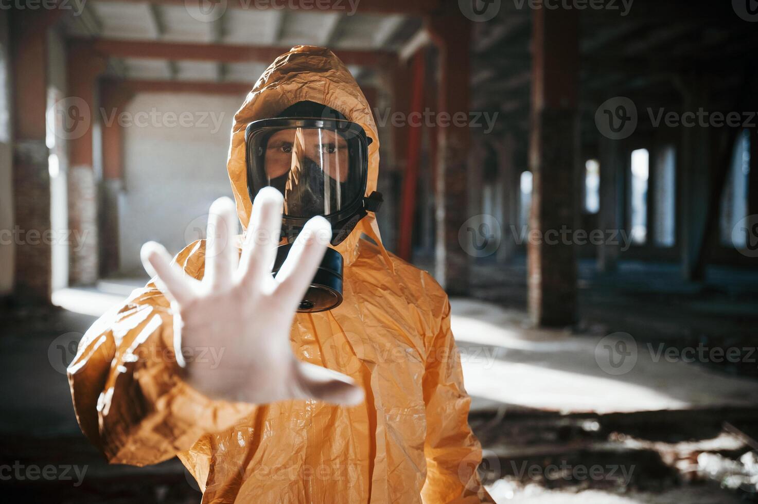 Stop sign by hand. Man dressed in chemical ,,protection suit in the ruins of the post apocalyptic building photo
