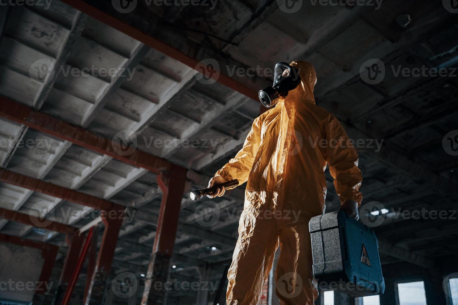 Indoors with flashlight. Man dressed in chemical protecti,on suit in the ruins of the post apocalyptic building photo