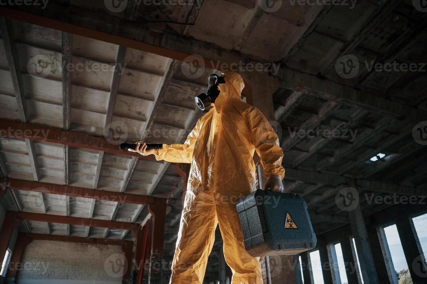 Using ,the flashlight. Man dressed in chemical, protection suit in the ruins of the post apocalyptic building photo