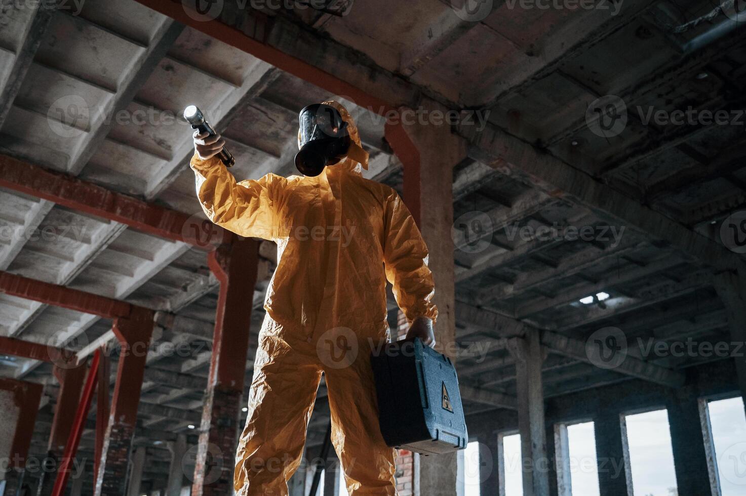 Indoors with flashlight. Man dressed in chemical, protection suit in the ruins of the post apocalyptic building photo