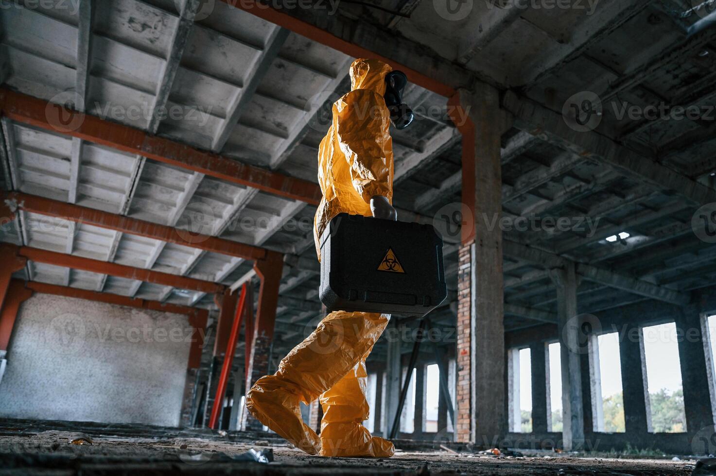 Walking with hard case. Man dressed in chemical, protection suit in the ruins of the post apocalyptic building photo