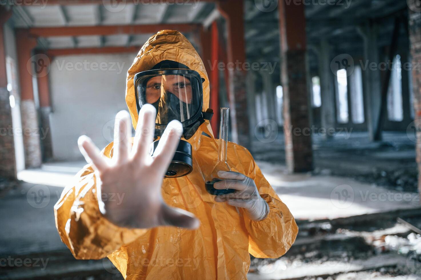 Stop sign by hand. Man dressed in ,chemical protection suit in the ruins of the post apocalyptic building photo