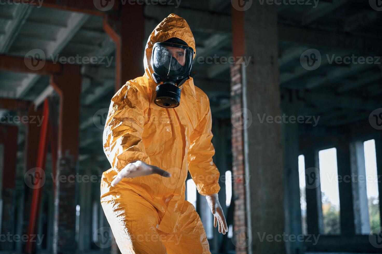Reaching for an object that is on the ground. Man dressed in chemical protection suit in the ruins of the post apocalyptic building photo