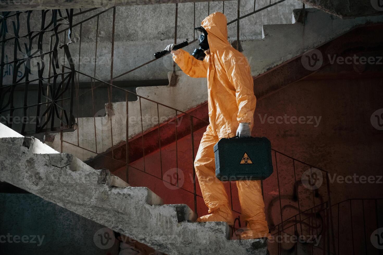 On stairs with flashlight and case. Man dressed in, chemical protection suit in the ruins of the post apocalyptic building photo