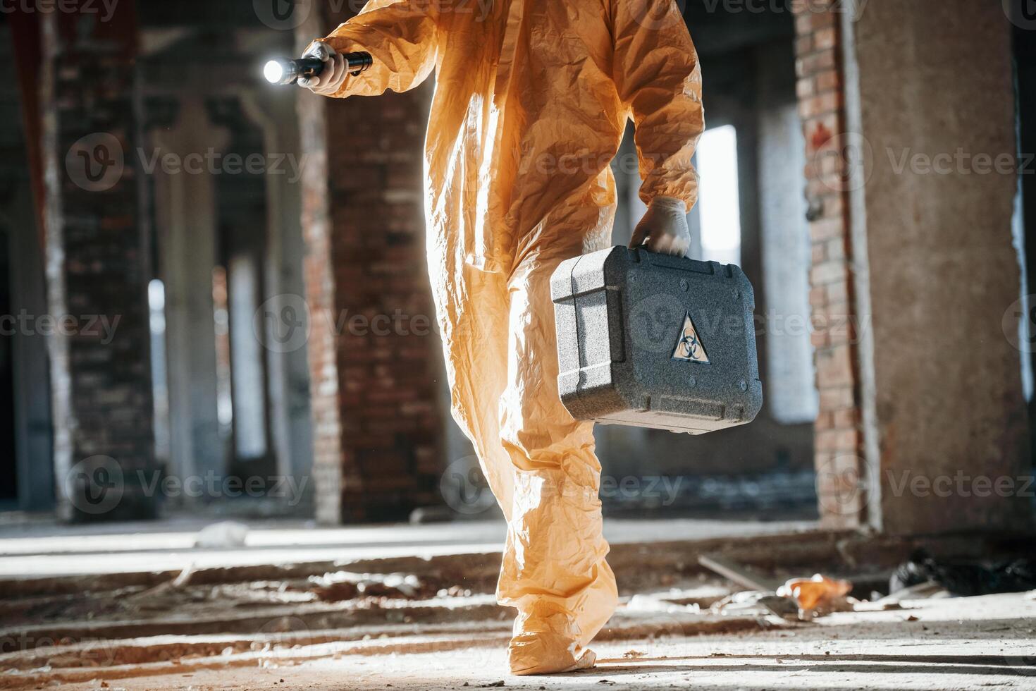 With flashlight. Man dressed in chemical protection suit in the ruins of the post apocalyptic building photo