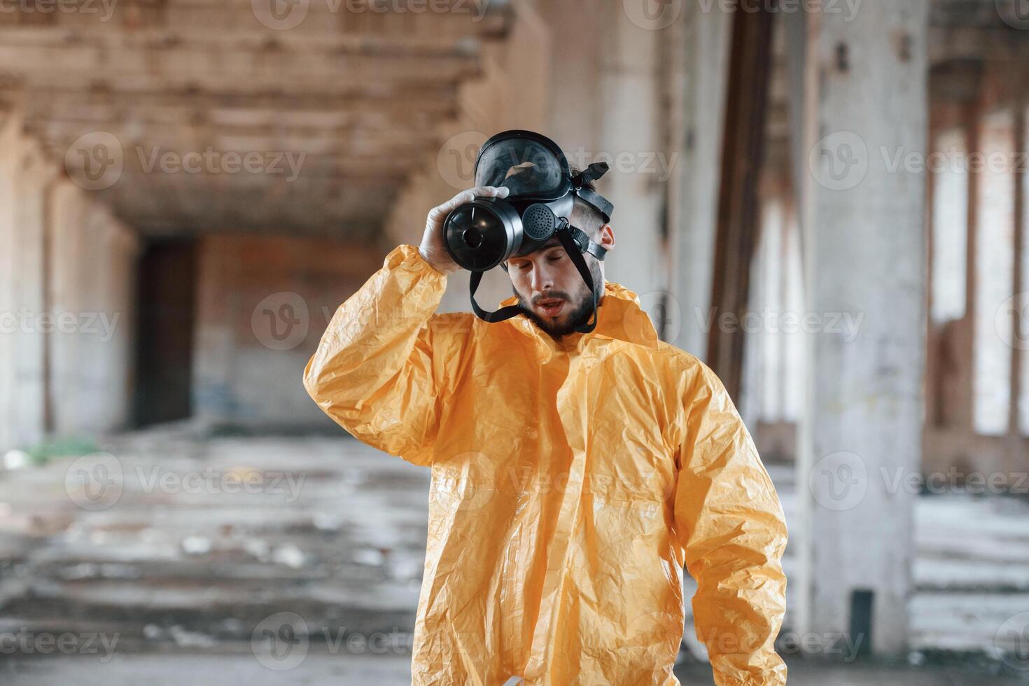 Taking off gas mask. Man dressed in chemical,, protection suit in the ruins of the post apocalyptic building photo