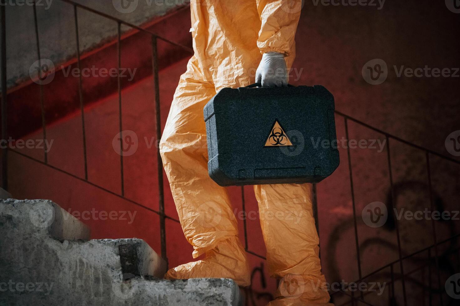 On ,stairs with flashlight and case.. Man dressed in chemical protection suit in the ruins of the post apocalyptic building photo