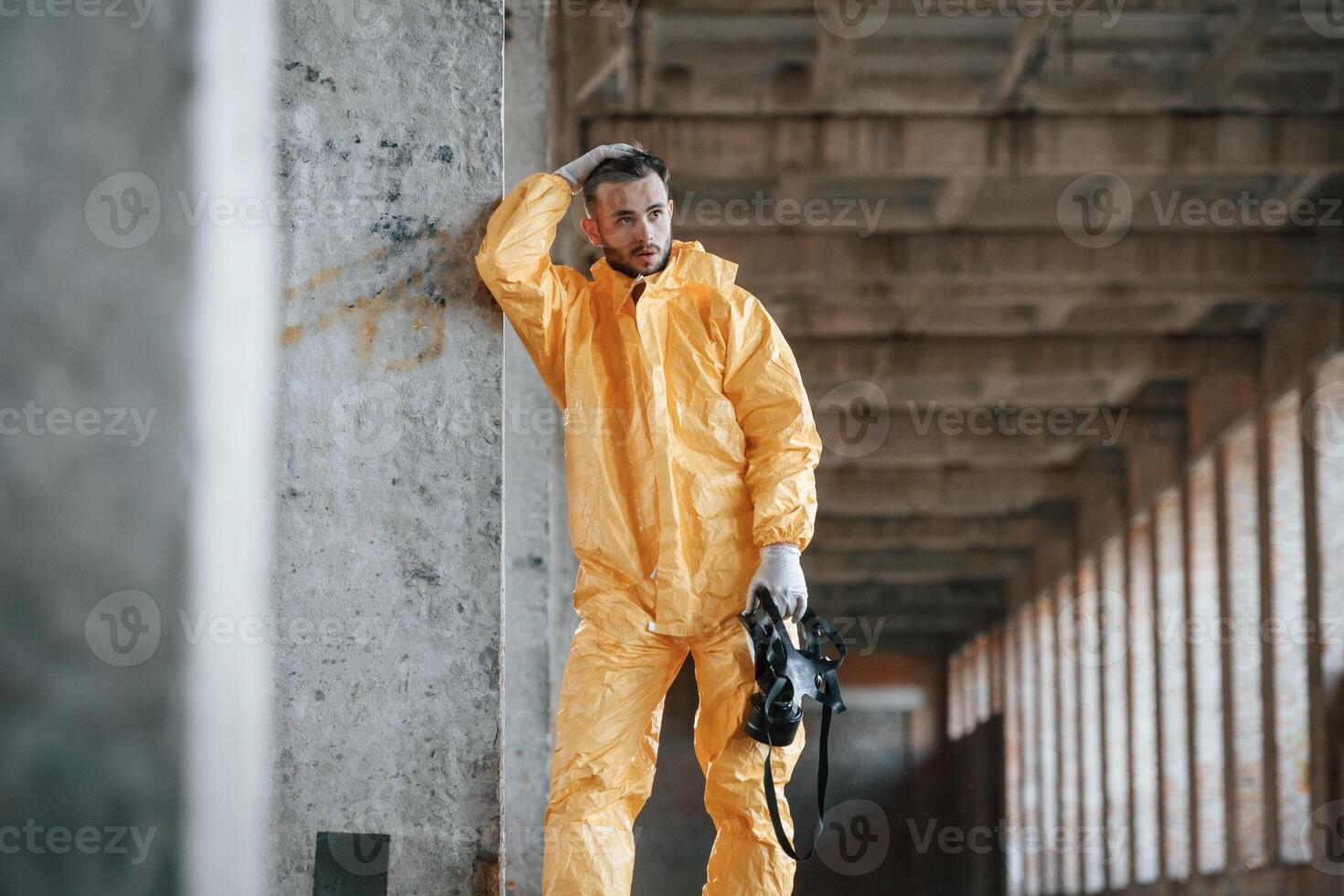 Tired,, frightened. Leaning on the wall. Man dressed in chemical protection suit in the ruins of the post apocalyptic building photo