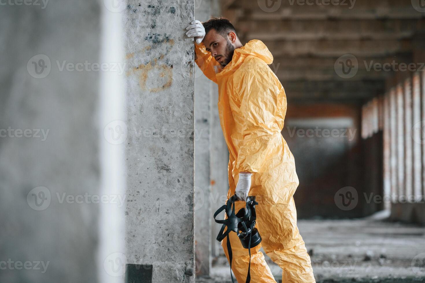 Tired, frightened. Leaning on the wall. Man dressed in chemical protection suit in the ruins of the post apocalyptic building photo