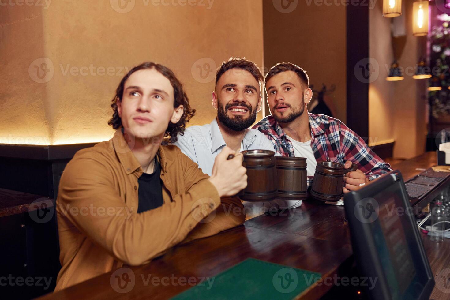 Sitting and, smiling.. Three friends are in the bar drinking beer and having a good time photo