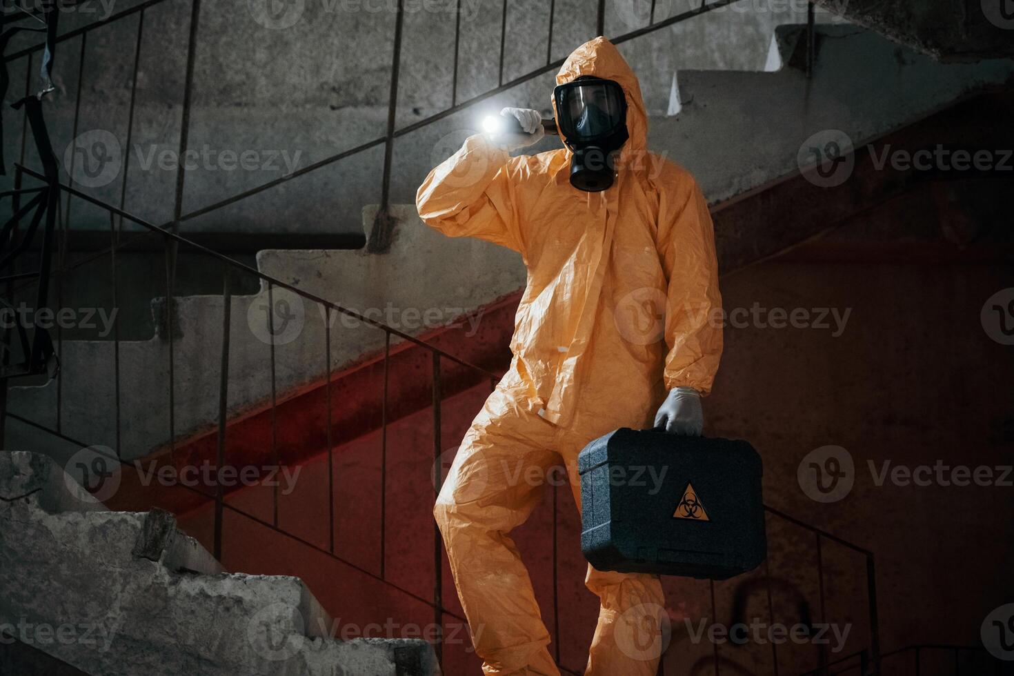 On ,stairs with flashlight and case. .Man dressed in chemical protection suit in the ruins of the post apocalyptic building photo