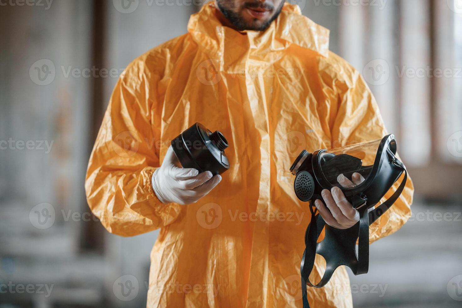 Holding a respirator. Man dressed in chemical protectio..n suit in the ruins of the post apocalyptic building photo