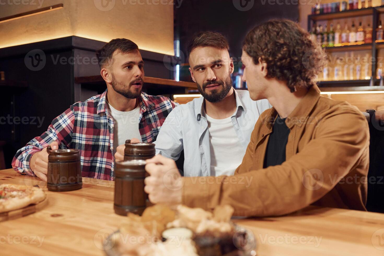 Having a ,conversation. Three friends are in the bar drinking beer and having a good time photo