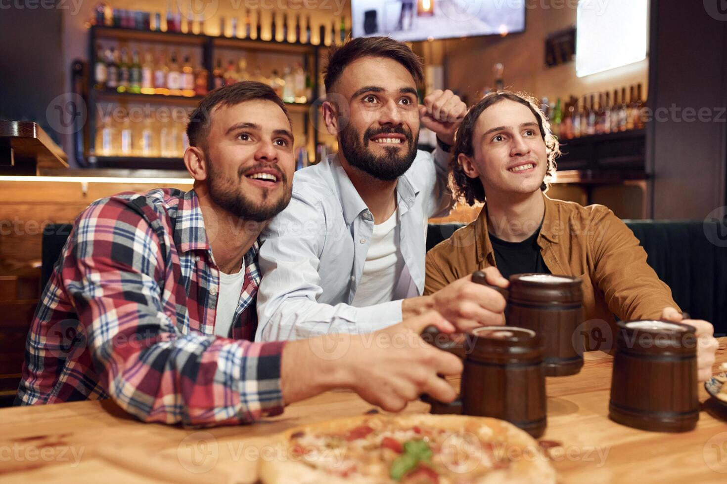 Front view. Soccer fans. Three friends are in the bar drinking beer and having a good time photo