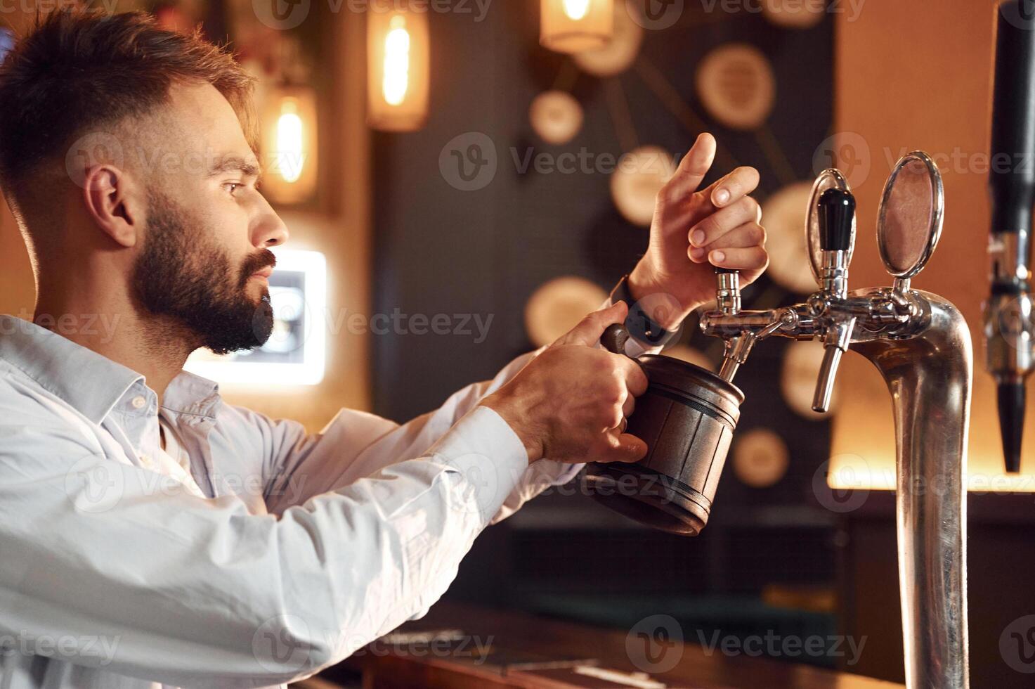Side view. Bartender pours beer. Man is working in. the bar photo