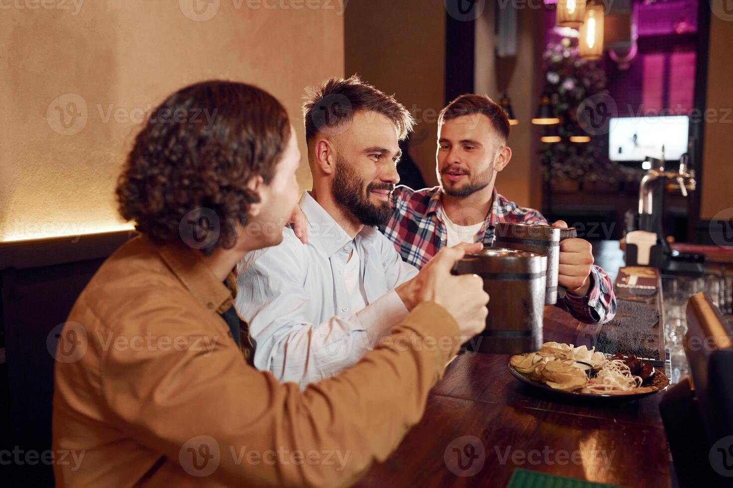 Raising up the mugs. Three, friends are in the bar drinking beer and having a good time photo