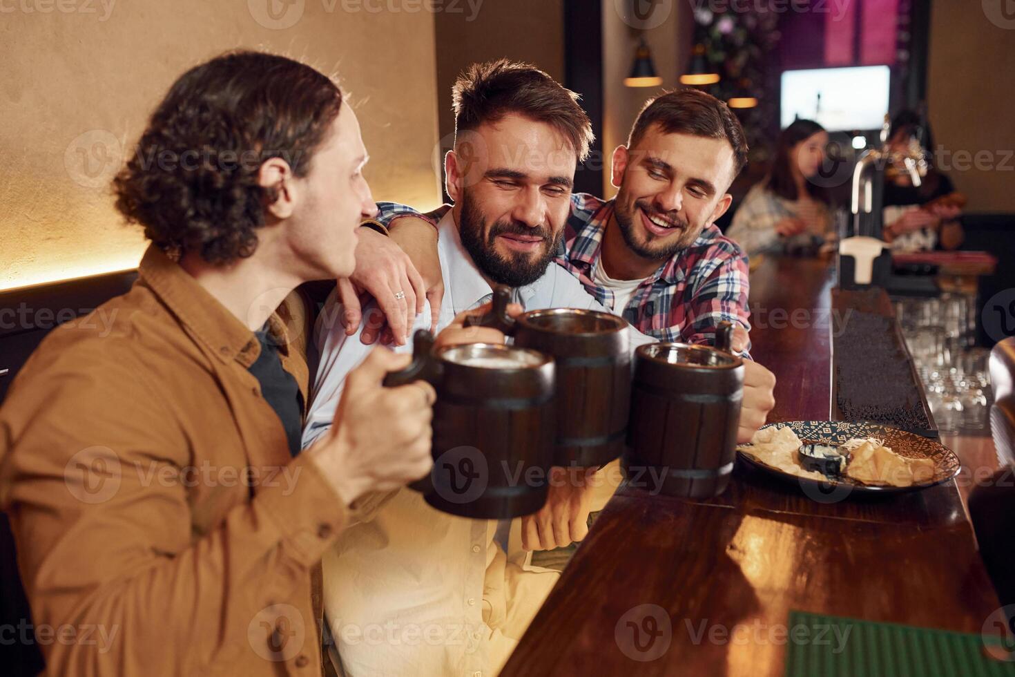 Sitting by the table. Three friends are ,in the bar drinking beer and having a good time photo