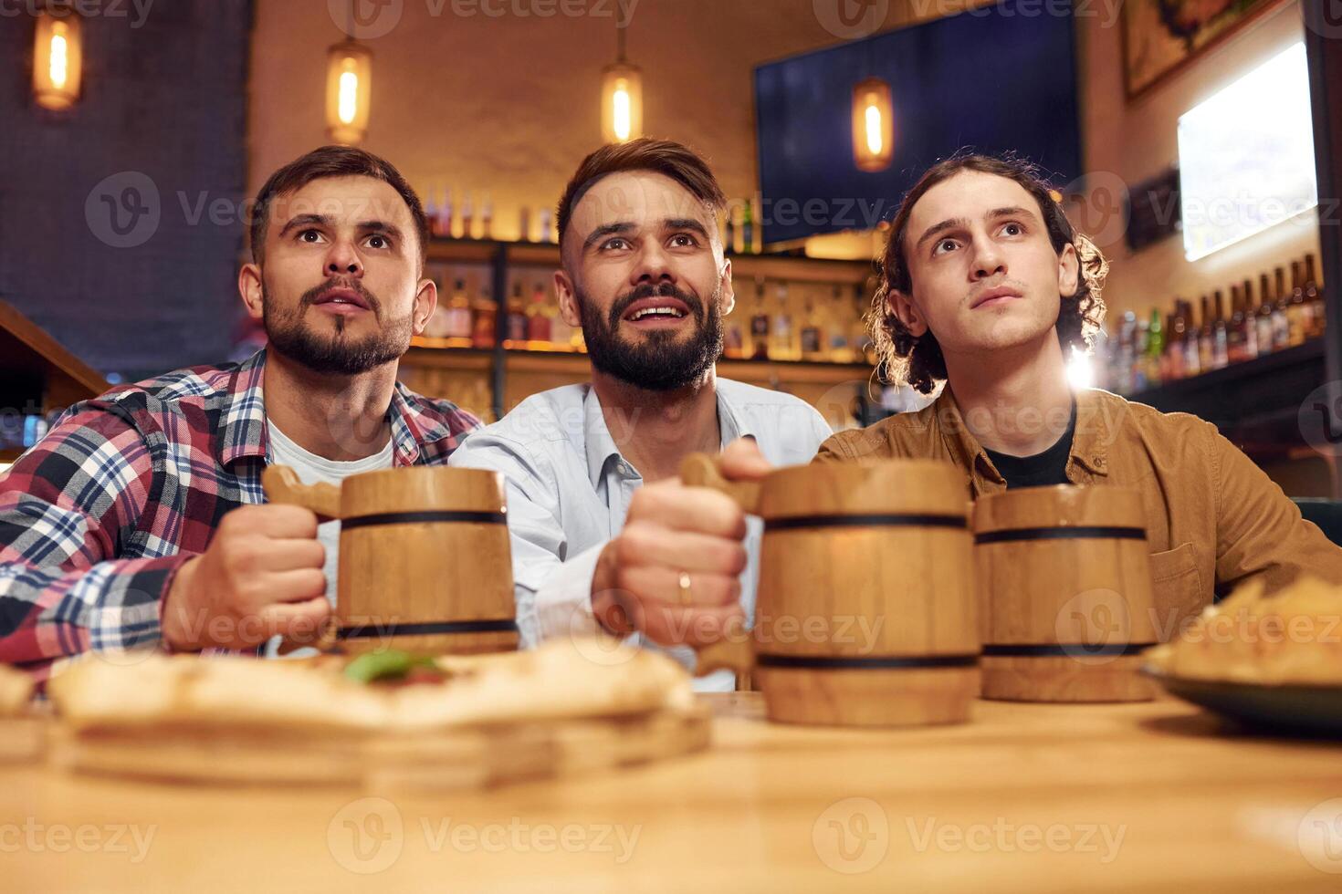 Watching TV. Three, friends are in the bar drinking beer and having a good time photo