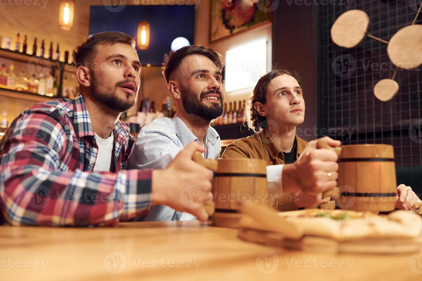Watching TV. Three friends ,are in the bar drinking beer and having a good time photo